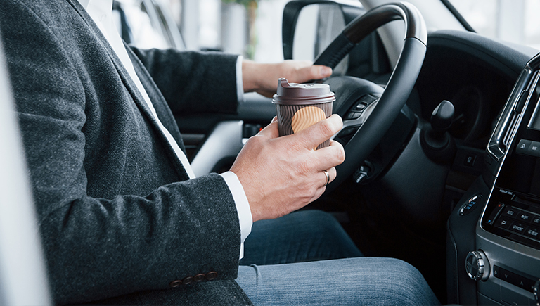 man in blazer holding cup of coffee in car